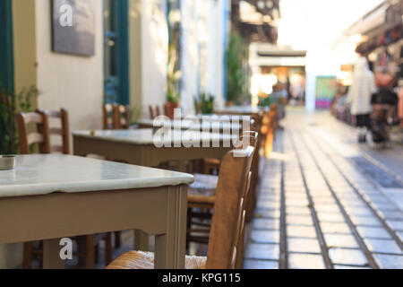 Athènes, Grèce. Taverne grecque tables et chaises vides dans une rangée, le flou d'arrière-plan du marché et des piétons Banque D'Images