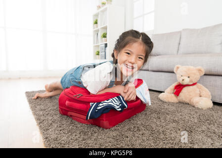 Les jeunes enfants beauté girl lying on assurance valise essayant de fermer et looking at camera quand elle voyage d'emballage buggage à la maison. Banque D'Images