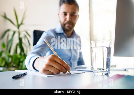 Jeune homme d'affaires dans son bureau d'écrire quelque chose avec un crayon. Banque D'Images