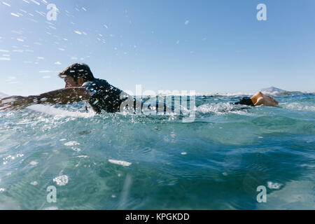 L'homme nage avec sa planche de surf en essayant d'attraper une vague dans la mer méditerranée. Banque D'Images