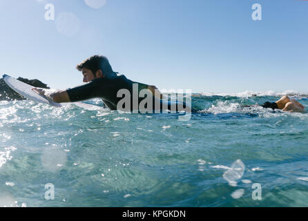 L'homme nage avec sa planche de surf en essayant d'attraper une vague dans la mer méditerranée. Banque D'Images