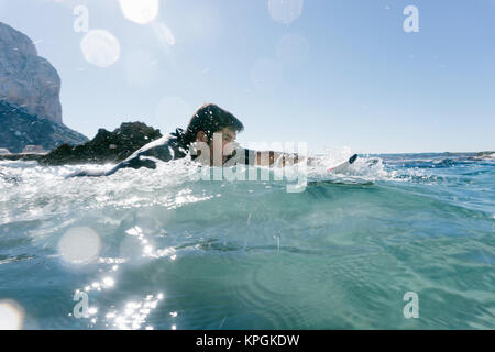 L'homme nage avec sa planche de surf en essayant d'attraper une vague dans la mer méditerranée. Banque D'Images