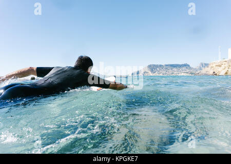 L'homme nage avec sa planche de surf en essayant d'attraper une vague dans la mer méditerranée. Banque D'Images