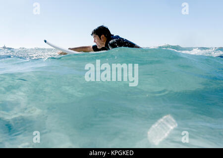 L'homme nage avec sa planche de surf en essayant d'attraper une vague dans la mer méditerranée. Banque D'Images