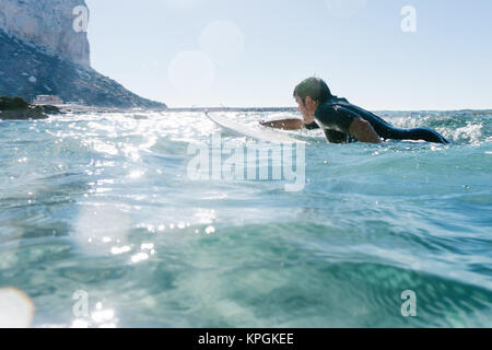 L'homme nage avec sa planche de surf en essayant d'attraper une vague dans la mer méditerranée. Banque D'Images