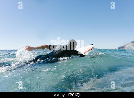 L'homme nage avec sa planche de surf en essayant d'attraper une vague dans la mer méditerranée. Banque D'Images