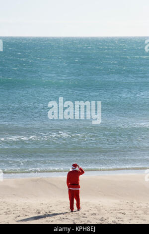 Santa Claus, vu de dos, debout sur la plage face à l'horizon Banque D'Images