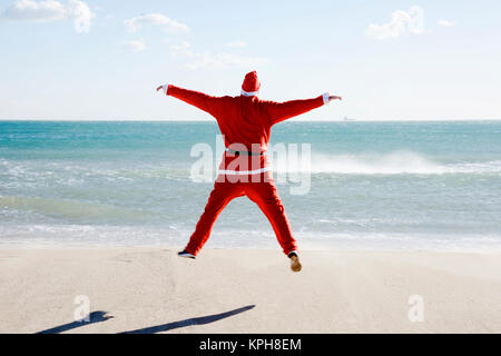 Santa Claus, vu de derrière, de sauter sur la plage face à l'horizon Banque D'Images