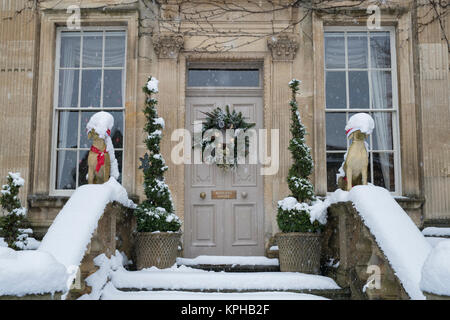 Chien de Noël et décoration guirlande porte des statues dans la neige à l'extérieur d'une maison de ville à Chipping Campden, Cotswolds, Gloucestershire, Angleterre Banque D'Images