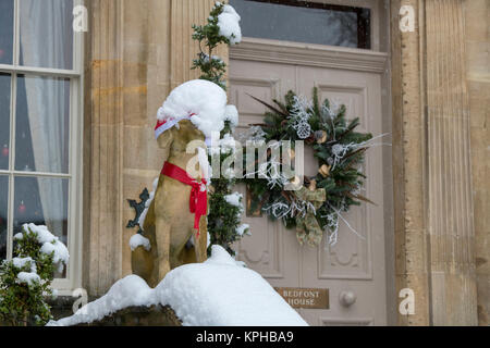 Statue de chien Noël Décoration guirlande de porte et dans la neige à l'extérieur d'une maison de ville à Chipping Campden, Cotswolds, Gloucestershire, Angleterre Banque D'Images