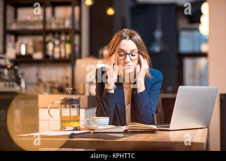 Jeune businesswoman having maux de tête tout en travaillant avec un ordinateur portable à l'intérieur moderne cafe Banque D'Images