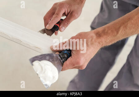 L'installation des moulures au plafond. Met de la colle sur des travailleurs de moulage de plastique pour plus de le fixer au plafond Banque D'Images