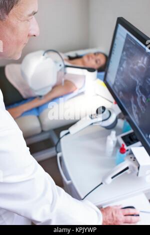Médecin Homme regardant un écran d'ordinateur, femme patient sur lit. Sur l'écran est visible d'une numérisation de la couche cornée de la peau du patient. Banque D'Images