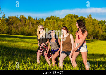 Un groupe de quatre amies randonnée pédestre à travers un champ dans un parc ; Edmonton, Alberta, Canada Banque D'Images