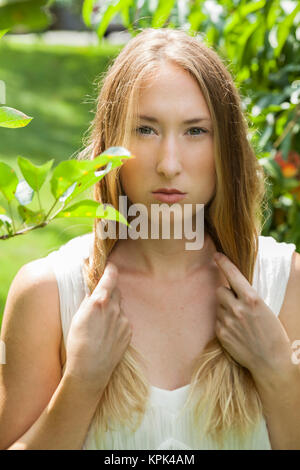 Belle jeune femme avec de longs cheveux blonds debout en vert feuillage ; California, United States of America Banque D'Images