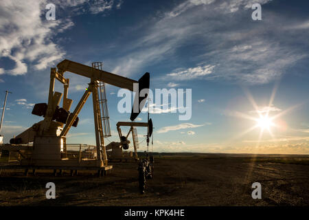 Une rétro-éclairé par l'pumpjack coucher de soleil sur l'Alberta Prairies avec ciel bleu et de nuages, à l'ouest d'Airdrie, Alberta, Canada Banque D'Images