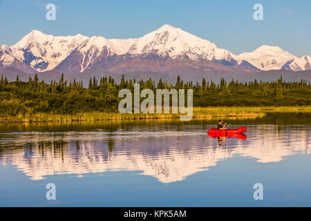 Un homme à travers les palettes Lac Donnelly dans un pack radeau avec Mt. Moffit et la chaîne de l'Alaska en réfléchissant sur l'eau ; l'Alaska, États-Unis d'Amérique Banque D'Images