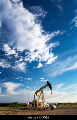 Pumpjack avec des nuages et ciel bleu au coucher du soleil, à l'ouest d'Airdrie, Alberta, Canada Banque D'Images