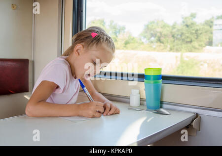 Fille dessine un stylo sur une feuille de papier dans un train de seconde classe Banque D'Images