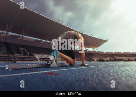 Vue arrière d'un athlète sur sa marque prêt à sprint sur une piste de course. Runner à l'aide d'un bloc de départ pour commencer sa course sur la piste de course dans un stade. Banque D'Images