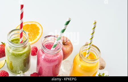 Ligne inclinée de apple, mangue et fraise boissons smoothie entouré par des cubes de glace et de divers morceaux de fruits sur fond gris avec copie espace Banque D'Images