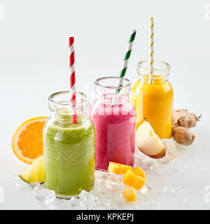 La ligne trois bols de apple, mangue et fraise boissons smoothie entouré par des cubes de glace et de divers morceaux de fruits sur fond gris Banque D'Images