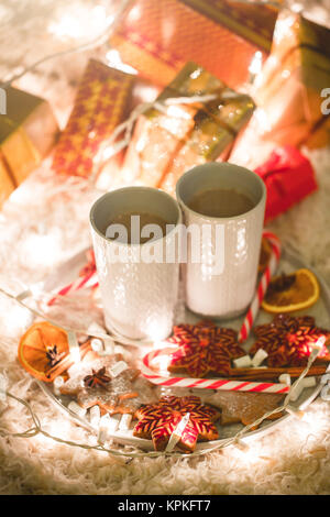 Boire un chocolat chaud avec des biscuits près de l'arbre de Noël Banque D'Images