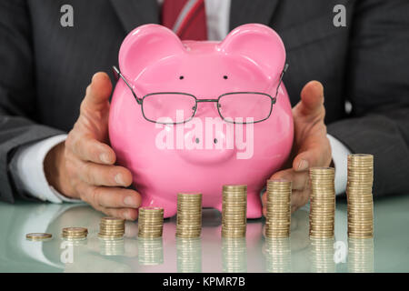 Businessman couvrant Tirelire Laughing At Desk Banque D'Images