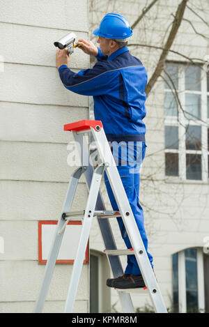 Technicien mâle debout sur l'escabeau Montage Caméra de surveillance Banque D'Images