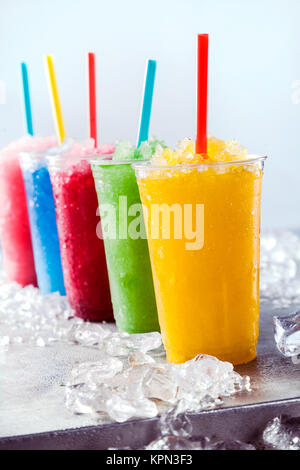 Nature morte de fruits congelés colorés Granita Slush en boissons à emporter en plastique tasses avec Pailles disposées en une rangée sur la surface de métal froid entouré par des cubes de glace Banque D'Images