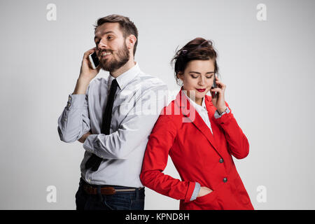 Concept d'entreprise. Les deux jeunes collègues détenant des téléphones mobiles sur fond gris Banque D'Images