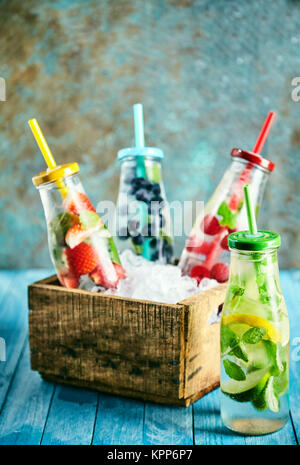 Plein de bouteilles d'eau glacée et de lime, citron, fraises, bleuets et framboises dans la petite boîte sur le dessus de table en bois Banque D'Images