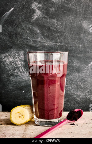 Un grand verre de smoothie acai exotique entre dans une tranche de banane et cuillère en plastique plus en arrière-plan Banque D'Images