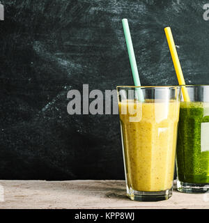 Amande sain et de la banane verte et colorée, cole ou kale frais, smoothies servi dans des grands verres d'une boisson savoureuse sur une table rustique, fond ardoise with copy space Banque D'Images