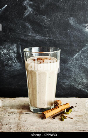 Grand Verre de délicieux chai latte avec une pincée de cannelle sur une table rustique à côté des bâtons de cannelle sur un fond noir Banque D'Images