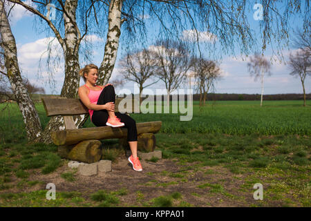 Blonde female jogger s'asseoir dehors sur un banc et prend un repos Banque D'Images