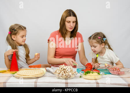 Maman montre deux jeunes filles à la table de cuisine comme la coupe tomato pizza Banque D'Images