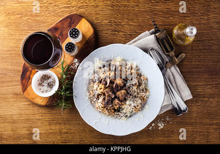 L'Italien risotto aux champignons et parmesan dans une assiette sur une table en bois. Un verre de vin rouge et d'huile d'olive. Banque D'Images