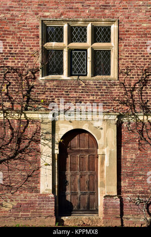 Une grande porte en chêne dans un mur de brique rouge entourée de plantes grimpantes avec une fenêtre en verre au plomb au-dessus au Blickling national trust house ou d'un bien. Banque D'Images