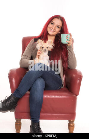 elle est assise sur une chaise avec un chien sur ses genoux et boit du café Banque D'Images