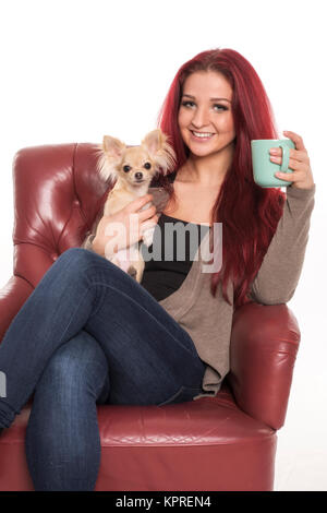 elle est assise sur une chaise avec un chien sur ses genoux et boit du café Banque D'Images