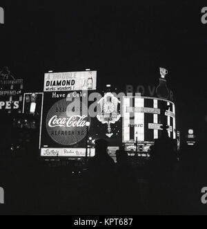 Années 1960, photo historique montrant les panneaux publicitaires et les slogans publicitaires éclairés la nuit à Piccadilly Circus, dans le West End de Londres, Angleterre, Royaume-Uni. Banque D'Images