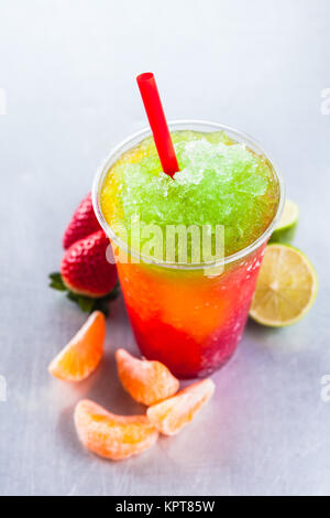 High Angle View of Colorful Rainbow Fruits surgelés en couches Granita Slush verre métal sur plastique en vente libre à emporter, tasse avec paille et entouré d'ingrédients de fruits frais Banque D'Images