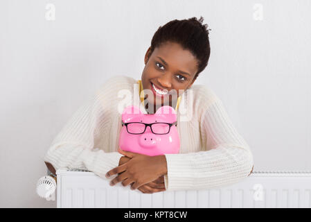 Woman with Piggybank se penchant sur radiateur Banque D'Images