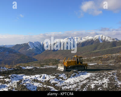 Tracteur à chenilles avec grederom sur fond de montagnes enneigées. Zone grederom d'alignement pour les besoins technologiques. Banque D'Images