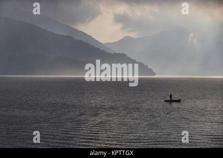 Pêcheur solitaire en bateau sur le lac Chuzenji pendant nuageux coucher du soleil avant que la pluie. 一人で中禅寺湖に釣り。 Banque D'Images