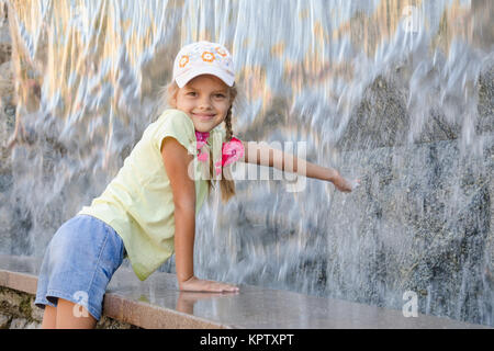 Fille dans des vêtements d'été avec un sourire étirant sa main à l'eau la cascade artificielle Banque D'Images