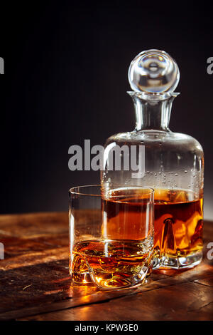 Verre de whisky en plus de carafe sur une table ronde en bois sur un fond noir Banque D'Images