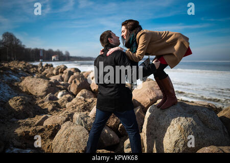 Jeune beau couple en vêtements élégants à la recherche à l'autre et prêt à baiser sur la côte en hiver Banque D'Images