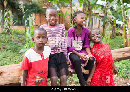 Lugazi, en Ouganda. 18 juin 2017. Un groupe d'enfants ougandais souriant assis sur un tronc d'arbre tombé. Banque D'Images